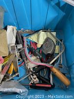 Top view of assorted hand tools including hacksaw, pliers, and screwdrivers in blue storage bin.