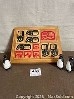 Full view of Haida art puzzle in wooden frame on gray background with three bobblehead penguins placed in front.