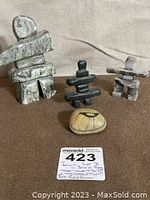 Three Inukshuk sculptures displayed with a small painted stone on brown fabric background and a lot tag showing item number and description