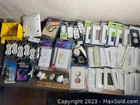 Photo showing a mixed lot of electrical parts including multiple duplex outlets, rocker switches, switch and outlet covers mostly white and new in box or wrapping.