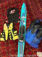 Photo showing the full water ski in blue with black bindings, two yellow adult life jackets, and a black Jetpilot wakeboard vest.