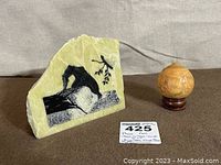 Bear artwork carved and inked on greenish stone slab with signature and oriental gourd seed pod sphere on wooden base.