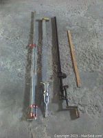 Three pipe bar clamps laid on the ground with a measuring stick for size reference.
