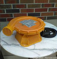 Full view of the yellow air blower, showing circular body, curved air outlet, power cord with switch, and label on top.