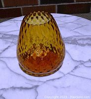 Amber glass vase photographed on a marble surface, showing the dimpled honeycomb texture and blunt sawtooth rim from an angled top view.