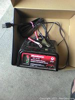 Black Motomaster battery charger with attached cables inside a cardboard box.