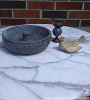 Image showing frosted heavy stone birdbath with a round shape, small raised middle post. Also shows dark metal bird mounted on ball base alongside vintage dove door stopper with distressed tan and white paint.