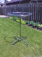 Round metal clothes rack standing upright outdoors on grass with lockable caster wheels visible on base.