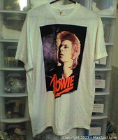 Full front view of white David Bowie t-shirt hanging, showing the large graphic print of David Bowie and orange 'Bowie' text.