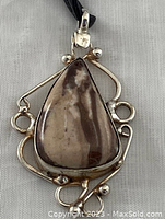 Front view of jasper pendant showing natural speckled jasper stone in triangular shape set in ornate 925 silver with decorative loops and beads, hanging from black cord.