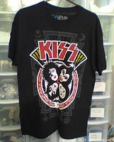 Front view of the black Kiss t-shirt showing the graphic of band members' faces inside a circular red and white emblem with 'KISS' in red letters above.