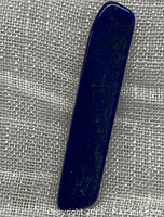 Polished lapis lazuli stone on a textured fabric background, showing deep blue color with natural flecks.