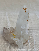 Natural quartz crystal cluster from Madagascar photographed from one angle on a beige fabric background.