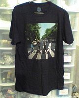 Full view of the black Beatles t-shirt laid out showing entire front including the Abbey Road album cover photo print in color.
