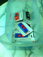 Top view of 10 USB rechargeable lighters in original packaging inside a plastic bin on a marble surface. Mix of red, blue, and black colors.