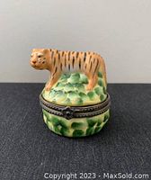 Front view of vintage small tiger ceramic jewelry box with metal hinge closure on leafy green base.