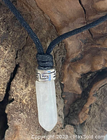 Close-up of the pointed white quartz crystal pendant with silver-tone Greek key patterned cap on black cord.