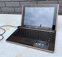Open ASUS laptop showing keyboard, touchpad, and screen with black bezel. Laptop is in good condition with visible sticker on palm rest.