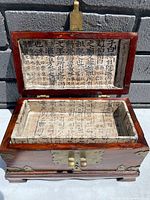 Top open view of rectangular wooden box showing interior lined with Chinese calligraphy on rice paper both on lid and base.