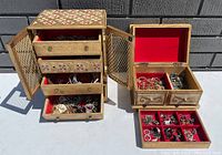 Two wooden jewelry boxes open to show multiple drawers with assorted jewelry inside, displayed outdoors on a surface