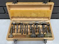 Open wooden case with 14 Forstner router bits arranged inside, showing bit sizes and foam padding in lid
