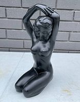 Front view of the black chalkware Art Deco style sculpture of a kneeling nude female figure with arms raised above her head.