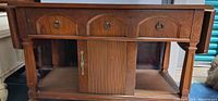 Front view of antique wooden tea cart showing three drawers, tambour cabinet door, side extension on left.