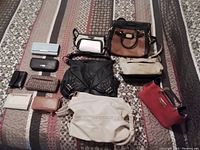 Photo showing an assortment of leather handbags and wallets in various colors and sizes arranged on a bedspread.