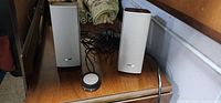 Pair of silver Bose speakers with wired control on wooden surface.