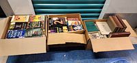 Three cardboard boxes filled with various books, showing variety and quantity