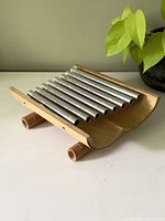 Front side view of bamboo musical instrument showing curved bamboo frame and metal pipes arranged horizontally.