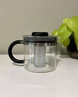 Bodum tea pot with black handle and lid, glass body, and transparent infuser inside.