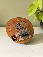 Front view of kalimba showing carved wooden top with floral design and metal tines.