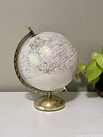 Front view of the white and gold globe with brass stand placed on a white surface, showing Europe and Africa regions.