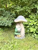 Side view of the gnome hugging the large mushroom statue in a garden setting with grass and foliage background.