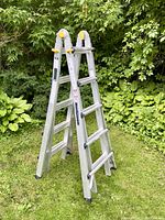 Full view of aluminum folding ladder set up in A-frame configuration on grass outdoors, showing rungs and locking tabs.