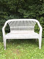 Front view of white plastic outdoor bench on grass, showing dirt and weathering.