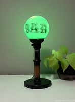 Vintage retro bar table lamp lit with green bulb, showing glowing 'BAR' lettering on round globe shade and black cylindrical base with brown aged patina.