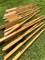 Set of 22 wooden balusters laid out on grass, showing both ends and details of wood grain and turned design.
