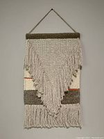 Full front view of the macramé wall hanging showing triangular and horizontal textured patterns with fringed tassels.