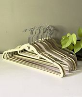 Side view of beige and grey velvet hangers stacked with metal hooks visible, showing their double-hung design and velvet texture.