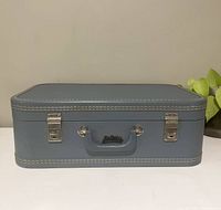 Front view of vintage blue suitcase showing latches and handle with stitching detail.
