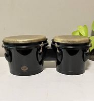 Front view of pair of black vintage bongo drums with natural drum heads, showing size difference and connection by wooden bridge.