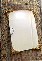 Full view of rectangular mirror on patterned rug showing four brass corners with decorative scroll and floral design.