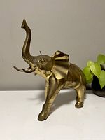 Front left side view of brass elephant figurine showing raised trunk and tusks with visible patina.