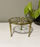 Front side view of the brass plant stand showing three tapered legs and round patterned top surface