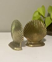 Front view of the two brass seashell bookends showing their different shell shapes, height, and base support.