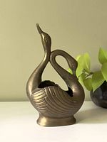 Front view of vintage brass planter shaped as two swans with intertwined necks and detailed feather patterns.