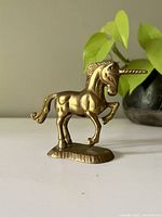 Side view of the brass unicorn figurine showing the raised front leg and head profile with detailed horn and mane.