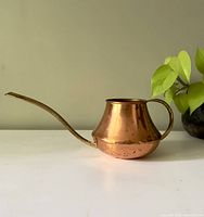 Side view of vintage copper watering can showing rounded body, curved spout, and handle.